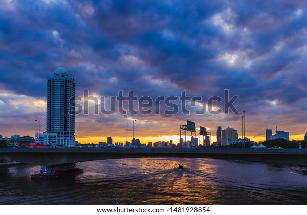 A boat is passing a bridge with a car running\
on a river in Bangkok,\
Thailand.