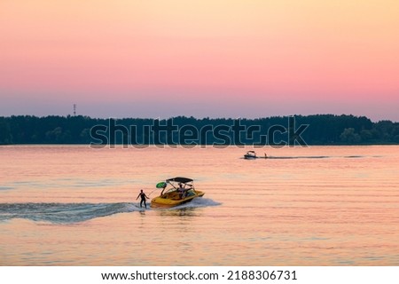 A boat pulls a person over the waves on a wakeboard. Wakeboarding at sunset.
