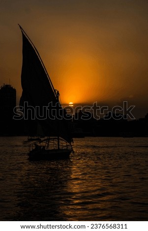 Silhouette einer ägyptischen Stadt mit Segelboot im Vordergrund und pastellrosa-lila farbenem Himmel, Sonnenuntergangsstimmung