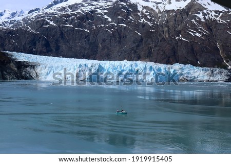 A boat sails in front of a glacier. The small boat in front of the massive glacier shows the glacier's size.