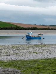 An Boat In Shallow Water At Low Tide. Hills Under A Cloudy Sky. Silt And Seaweed. Landscape.