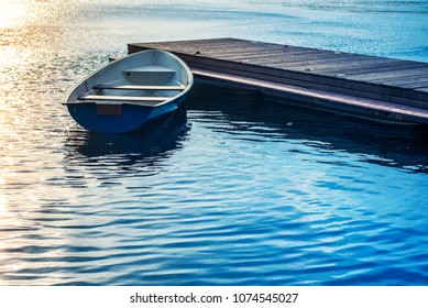 A boat tied to a wooden pier on the lake in the evening at sunset - Powered by Shutterstock