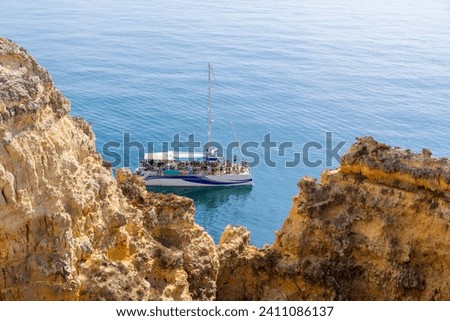 Boat with tourists on the beautiful coast of the Algarve region. Huge golden cliffs of the Algarve in Portugal.