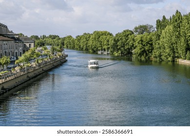 Un barco está viajando por un río Sharanta en coñac Francia. El agua es tranquila y clara. Hay árboles en la orilla del río