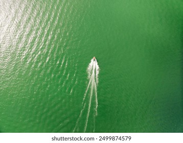 A boat is traveling through the water, leaving a wake behind it. The water is a deep, green color, and the sky is clear and bright. The scene is peaceful and serene - Powered by Shutterstock