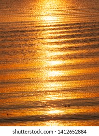 A Boat Wake During An Orange Sunset Leaves A Pattern On The Water