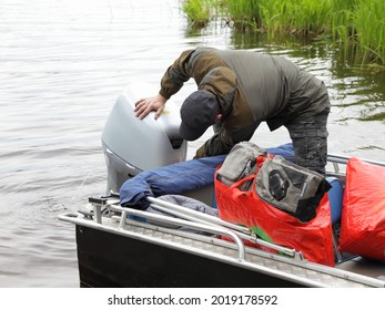 Boater man checks the hood of a 50 hp four stroke broken outboard motor on transom of boat near grass, repair and maintenance boat engine