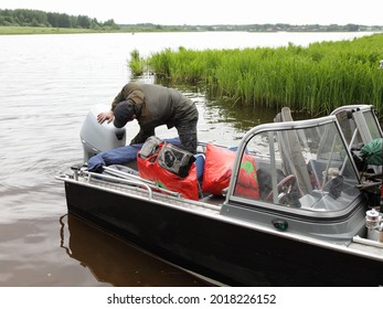 Boater Man Repairs The 50 Hp Four Stroke Outboard Motor On Transom Of Boat Near Shore Grass, Repair And Maintenance Boat Engine