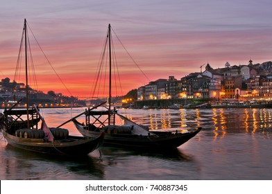 Boats carrying barrels of porto wine seen docking at river bank at sunset time at Porto, Portugal. The sky was burning red. 