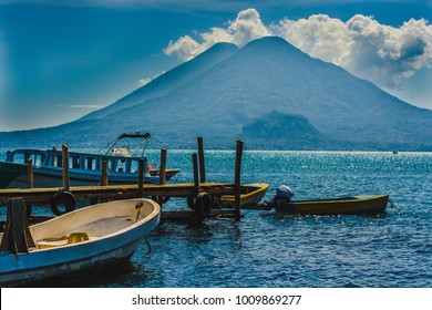 Boats Docked In Lake Atitlán, Guatemala With Volcanoes In The Background.