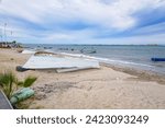 Boats overturned on sand on coastal beach, others in waters of Sea of Cortez, seascape with peninsula and horizon against blue sky with white clouds in background, La Paz, Baja California Sur Mexico