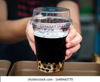 At Boba Tea Store,  Saleman Is Handing A Glass Of Chocolate Boba Tea With Ice Towards Cumstomer. Serving A Beverages To Customers. 