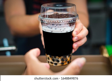 At Boba Tea Store, Saleman Is Handing A Glass Of Chocolate Boba Tea With Ice Towards Cumstomer. Serving A Beverages To Customer's Hand.

