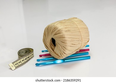 A bobbin of yarn lies on hooks with Measuring tape. Isolated side view of a textile reel on a white background. Straw yarn and colorful hooks. Designer measuring tape, centimeter. - Powered by Shutterstock