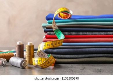 Bobbins with threads, measuring tape and stack of colorful fabrics on table. Tailoring accessories