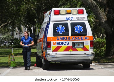 BOCA RATON, FLORIDA / USA - MAY 30 2020 -  Smiling Female EMT In Blue Shirt Holding Face Mask During Coronavirus Pandemic Walks In Front Of Ambulance Parked At Boca Raton Community Hospital.