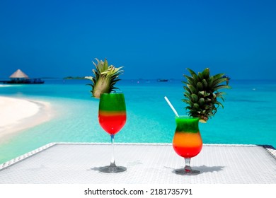 Bocal of fruity cocktail on a beach table. Maldives Island landscape. Tropical fresh juices on white sandy beach. Colorful fruity drink on Maldives landscape.
