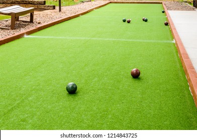 Bocce Balls Surround The Polina Which Is A Small White/yellow Ball On A Green Bocce Court Outdoors.