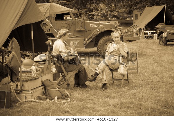 BOCONNOC, CORNWALL, ENGLAND, UK - JULY 30, 2016:\
Women In American World War Two Costume Sitting Drinking in Army\
Camp Re-enactment. Sepia and Grain Effect added for Vintage Look.\
Editorial Use Only