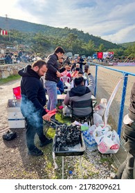 Bodrum, Turkey - 8th Jan. 2022: Man Preparing The Carcoal BBQ Outside The Sports Arena. Local People Gather For Picnic And Chatting, Laughing And Watching The Traditional Camel Wrestling Fight. 