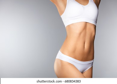 Körperpflege. Schöne Frau in Form mit feinem, schlankem Körper, gesunde, weiche Haut in weißen Bikini-Panties auf grauem Hintergrund. Nahaufnahme Frauenkörper in Unterwäsche. Gesundheits- und Ernährungskonzepte. Hohe Auflösung