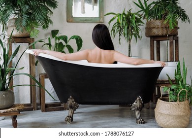 Body care concept. Back view of young adult woman taking bath in comfortable bathroom with green houseplants at classic interior. Graceful and naked girl enjoying morning routine procedure - Shutterstock ID 1788076127