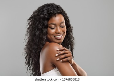 Body Care Concept. Portrait Of Beautiful African American Woman Touching Her Soft Skin On Shoulder Over Grey Background, Free Space