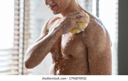 Body Care Concept. Smiling Man With Muscles Taking Shower Using Sponge