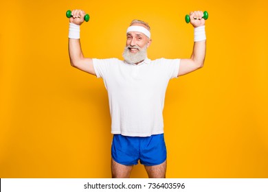 Body care, hobby, weight loss lifestyle. Cheerful cool grandpa with humor grimace exercising holding equipment up, lifts it with strength and power, wearing blue sexy shorts, so hot!