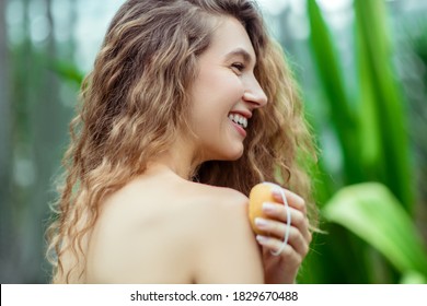 Body care. Naked woman holding a bar of orange soap and smiling