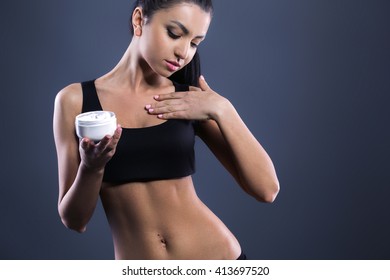 Body care. Studio shot of beautiful young woman with dark brown hair. Woman using body cream