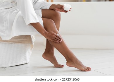 Body Care. Unrecognizable black woman applying moisturising cream on legs while making beauty routine at home, african american female wearing white silk robe using nourishing lotion, copy space - Powered by Shutterstock
