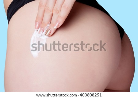 Body care. Woman applying cream on legs and buttocks. girl in a black thong, athletic ass. studio shot on a blue background