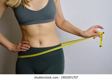 A body centimeter in the hands of girl in tracksuit after a workout or fitness session. Measurement of body volume. Sports waist. Healthy lifestyle, physical activity. Controlling figure while dieting