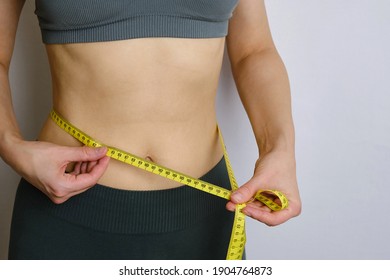 A body centimeter in the hands of girl in tracksuit after a workout or fitness session. Measurement of body volume. Sports waist. Healthy lifestyle, physical activity. Controlling figure while dieting