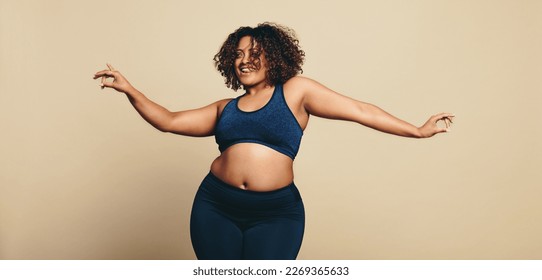 Body confident young woman dancing in sportswear, showing off her sportiness and flexibility. Fit plus size woman having fun as she expresses her body positivity in a studio.