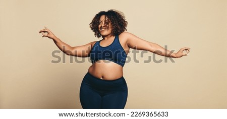 Body confident young woman dancing in sportswear, showing off her sportiness and flexibility. Fit plus size woman having fun as she expresses her body positivity in a studio.