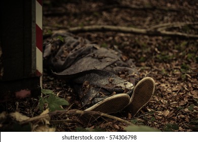 Body Of A Dead Person Wrapped In A Blanket Lying In Forest Detritus Half Covered By Leaves With Focus To The Feet In Sneakers