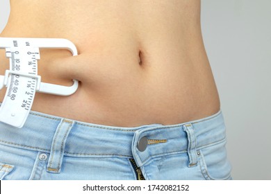 Body fat calipers, woman measuring subcutaneous percentage of fat on her belly. Young woman using skinfold calipers.