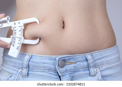 Body fat skinfold calipers, woman measuring subcutaneous percentage of fat on her belly.