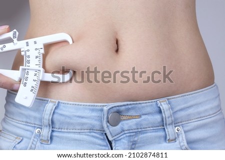 Body fat skinfold calipers, woman measuring subcutaneous percentage of fat on her belly.
