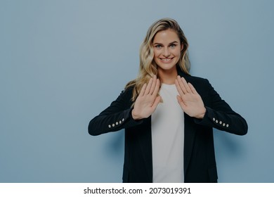 Body Language Concept. Smiling Polite Young Woman Dressed In Black Blazer Over White Tshirt Keeping Hands In Stop Gesture, Saying No Or Refusing Proposal While Standing Isolated Over Color Background