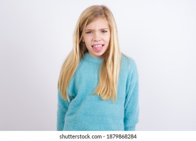 Body Language. Disgusted Stressed Out Cute Caucasian Kid Girl Wearing Blue Knitted Sweater Against White Wall, Frowning Face, Demonstrating Aversion To Something.