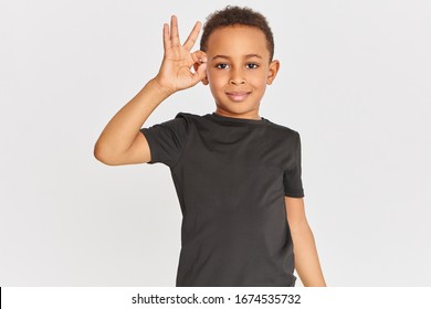 Body language. Portrait of friendly looking positive dark skinned little boy in t-shirt connecting fore finger and thumb making approval gesture, showing okay sign, saying Everything is fine