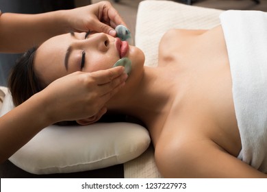 Body Massage On Facial Face Of Mix Race Caucasian Asian Woman, Therapist Spa Body Woman Hands Treatment On Customer With Chakra Balancing Massage Scrub Hot Jade Stone Effect Inner Emotion Stress Mind