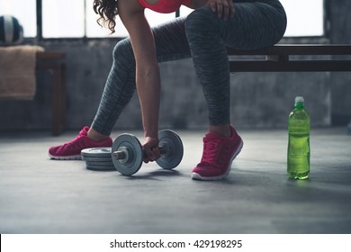 Body and mind workout in loft fitness studio. Closeup on fitness woman taking dumbbell from the floor in urban loft gym