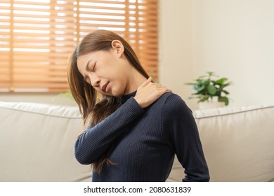 Body muscles stiff problem, asian young attractive woman, girl pain with back pain ache from work, holding massaging rubbing shoulder hurt or sore, painful sitting on sofa at home. Healthcare people. - Shutterstock ID 2080631839