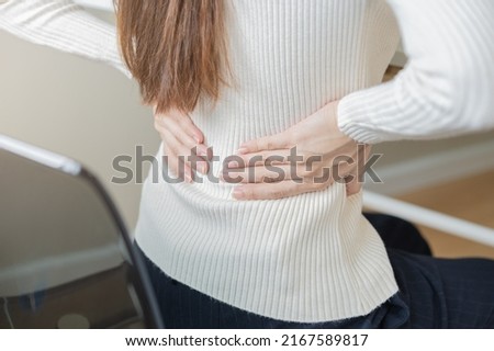 Body muscles stiff problem, asian young attractive woman, girl pain with back pain ache from computer work, holding massaging rubbing, hurt or sore while sitting on chair at home. Healthcare people.