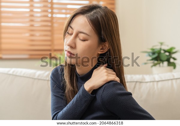 Body muscles stiff problem, asian young\
attractive woman, girl pain with back pain ache from work, holding\
massaging rubbing shoulder hurt or sore, painful sitting on sofa at\
home. Healthcare people.