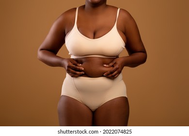 Body Neutrality Concept. Closeup Cropped View Of Unrecognizable Chubby African American Woman In Underwear Holding Fat Fold Love Handles On Her Belly, Standing Isolated Over Brown Studio Background